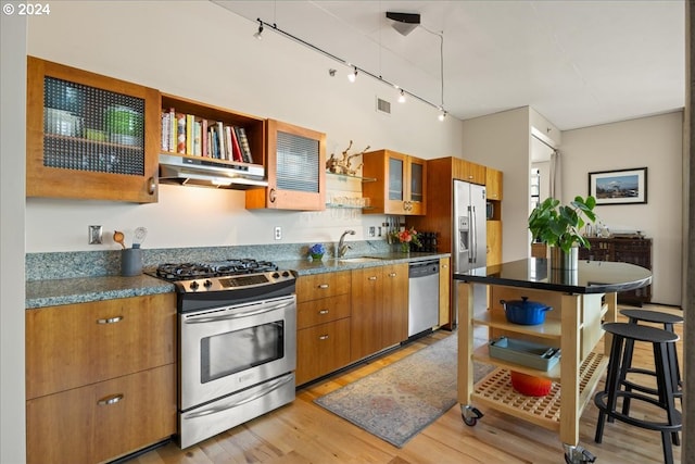 kitchen featuring sink, light hardwood / wood-style flooring, rail lighting, stainless steel appliances, and a kitchen bar