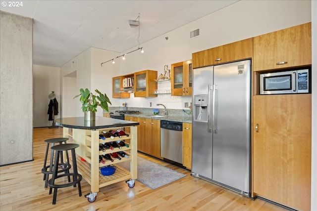 kitchen featuring sink, light hardwood / wood-style flooring, a breakfast bar, appliances with stainless steel finishes, and track lighting