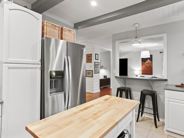 kitchen featuring light tile patterned floors, wooden counters, stainless steel fridge, pendant lighting, and white cabinets