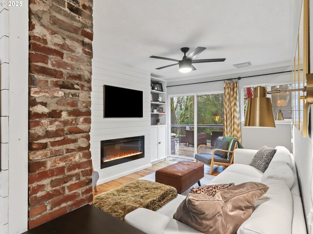 living room with ceiling fan, a large fireplace, and light hardwood / wood-style flooring