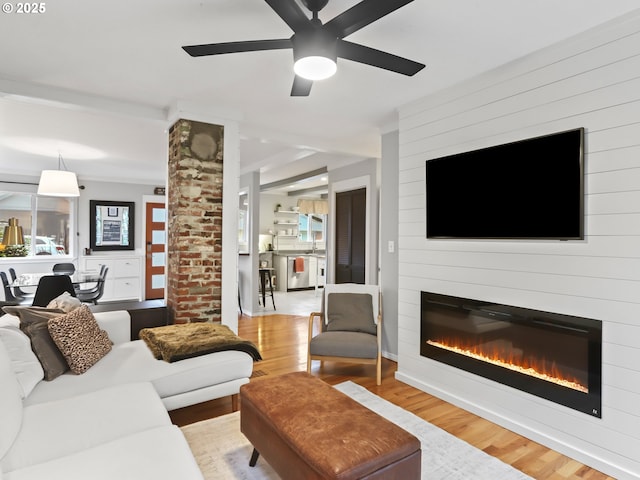 living room with ceiling fan, a large fireplace, and light wood-type flooring