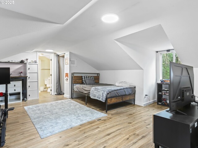 bedroom featuring light hardwood / wood-style floors, connected bathroom, and vaulted ceiling