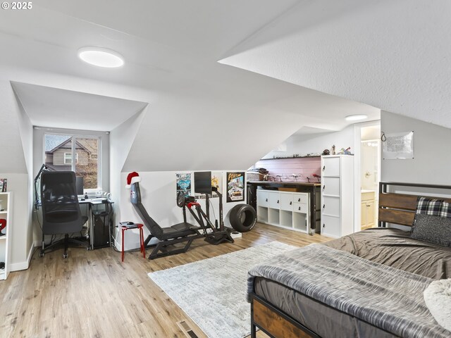 bedroom featuring light wood-type flooring, lofted ceiling, and connected bathroom