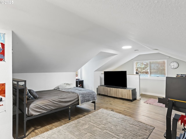 bedroom with a textured ceiling, hardwood / wood-style flooring, and lofted ceiling