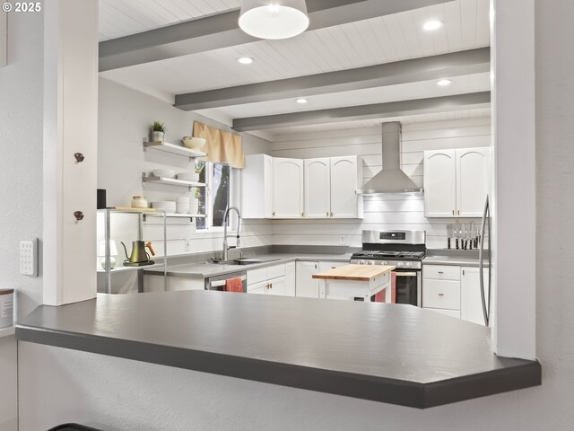 kitchen featuring kitchen peninsula, wall chimney exhaust hood, beamed ceiling, gas stove, and white cabinetry