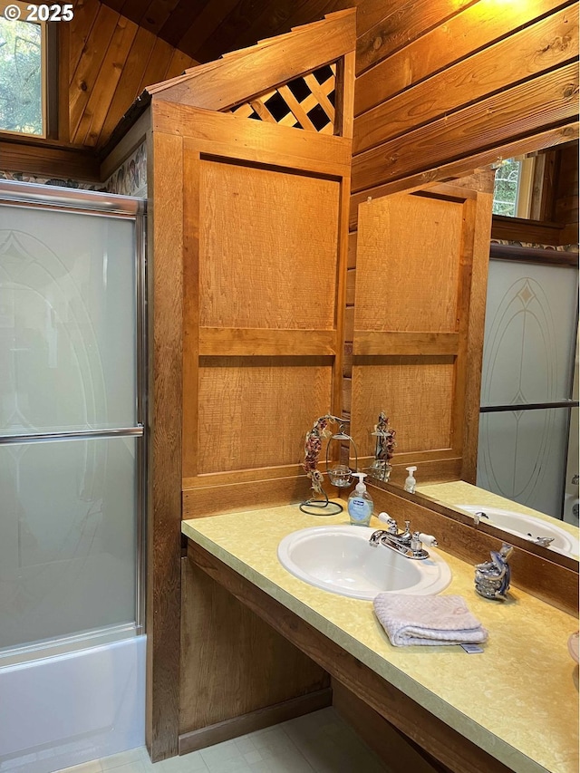 bathroom featuring sink, tile patterned flooring, shower / bath combination with glass door, and wooden walls