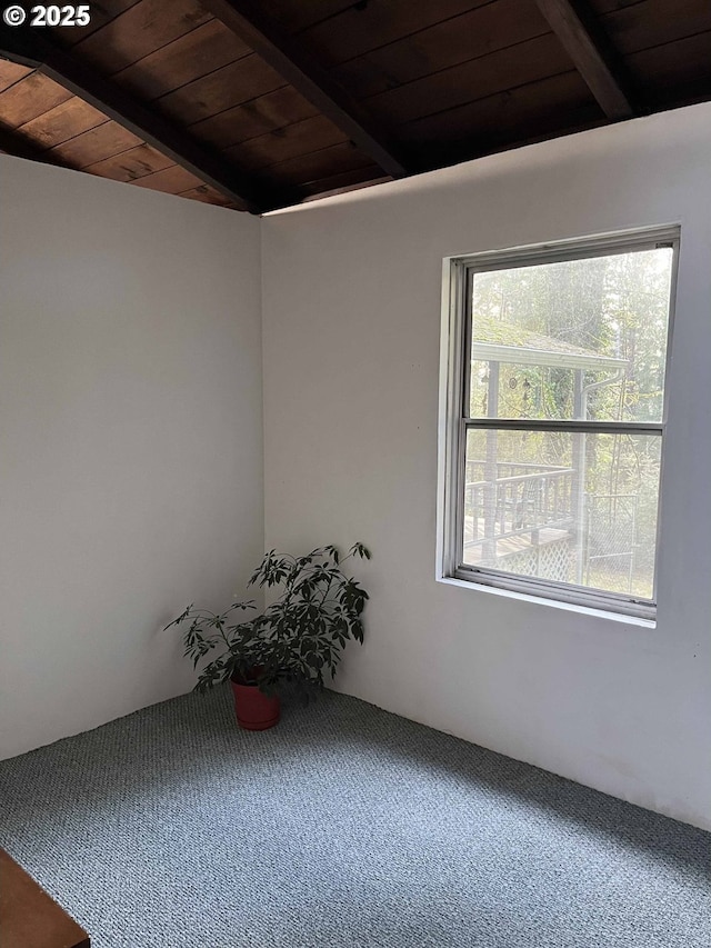 carpeted empty room featuring vaulted ceiling with beams and wood ceiling