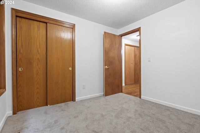 unfurnished bedroom featuring a textured ceiling, a closet, and light carpet