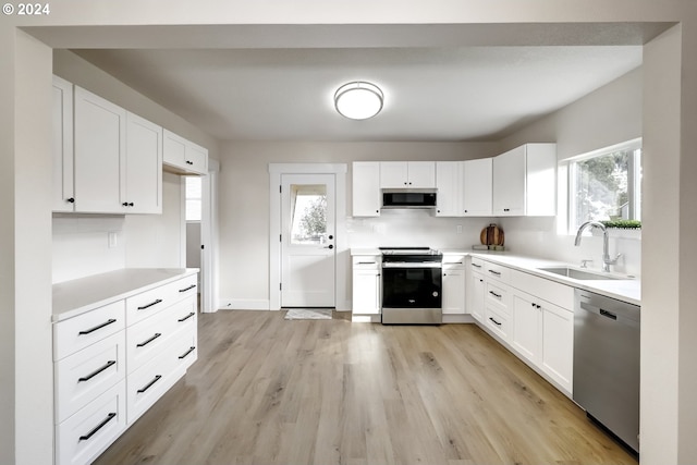 kitchen featuring white cabinets, a sink, light wood-style floors, light countertops, and appliances with stainless steel finishes