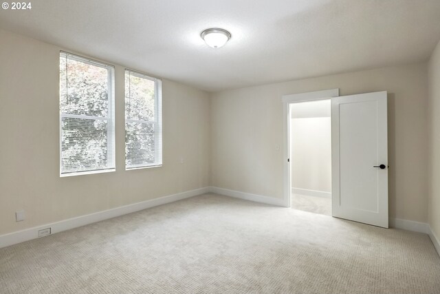 spare room featuring light colored carpet and baseboards