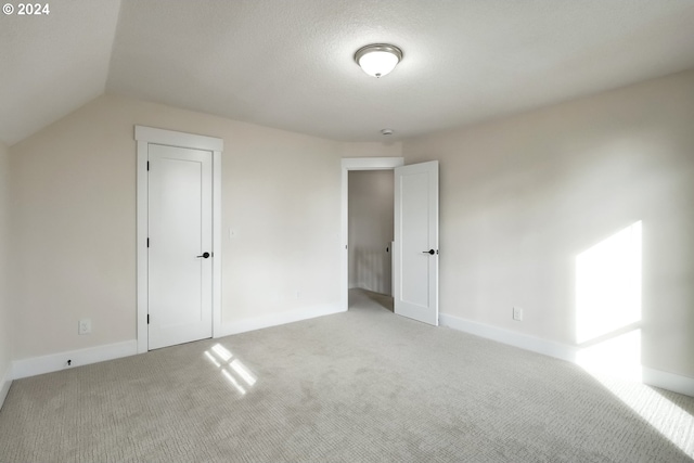 interior space with a closet, light carpet, a textured ceiling, and lofted ceiling