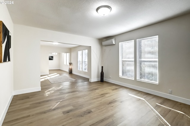 unfurnished living room featuring an AC wall unit, a textured ceiling, and wood-type flooring