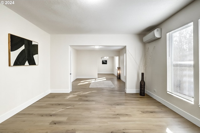 spare room with light wood-type flooring, baseboards, and an AC wall unit