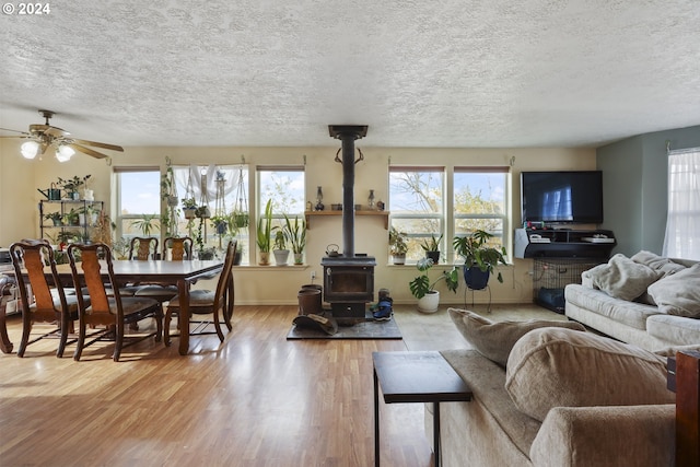 living room with ceiling fan, wood-type flooring, a textured ceiling, and a wood stove