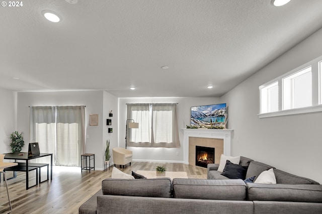 living room with light wood-type flooring, a textured ceiling, and a tile fireplace