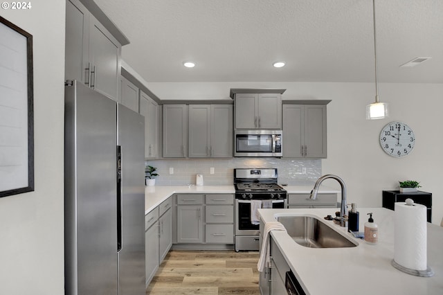 kitchen with light wood-type flooring, tasteful backsplash, sink, appliances with stainless steel finishes, and decorative light fixtures