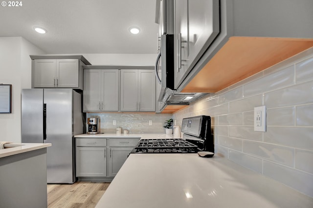 kitchen with tasteful backsplash, stainless steel fridge with ice dispenser, light hardwood / wood-style flooring, gray cabinetry, and black stove