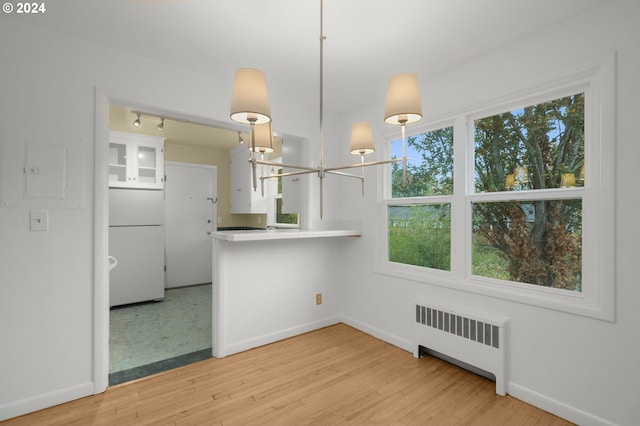 interior space with decorative light fixtures, white fridge, light hardwood / wood-style floors, white cabinets, and radiator heating unit