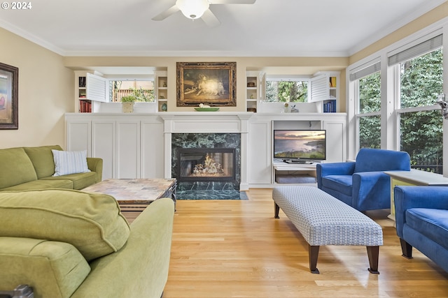 living room featuring a premium fireplace, light hardwood / wood-style floors, crown molding, ceiling fan, and built in shelves