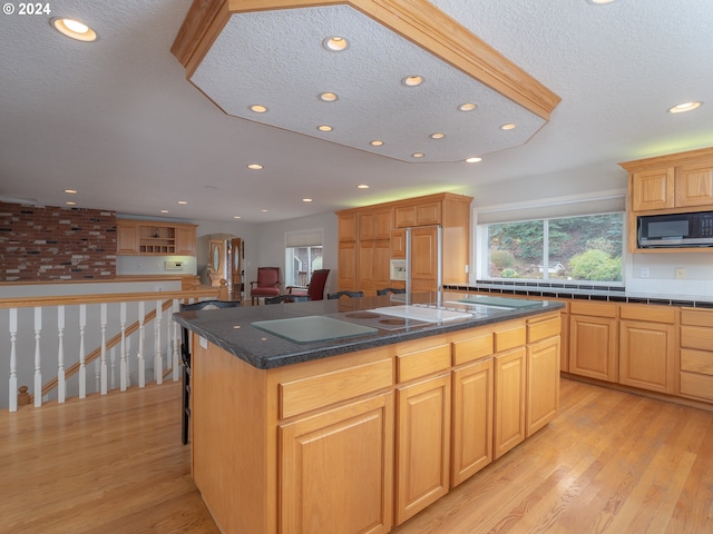 kitchen with light brown cabinetry, a center island with sink, light hardwood / wood-style floors, and a textured ceiling