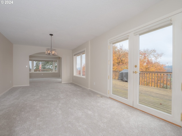 carpeted spare room featuring a wealth of natural light, a textured ceiling, and a notable chandelier