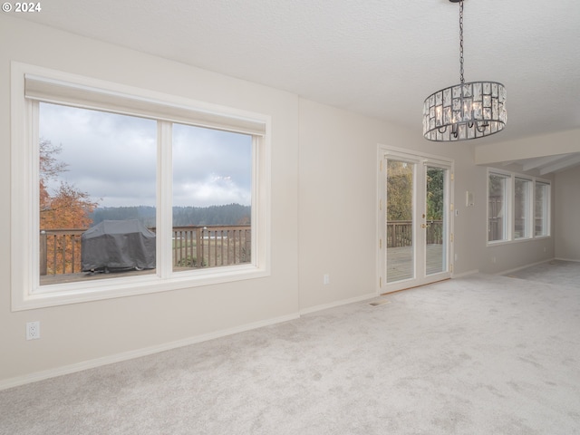 carpeted empty room with french doors, plenty of natural light, a chandelier, and a textured ceiling