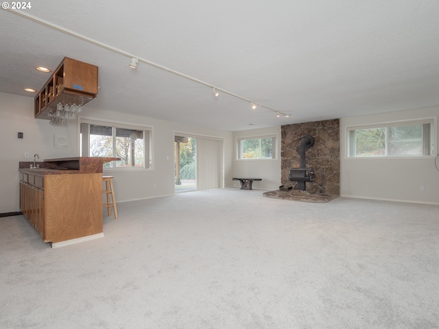 unfurnished living room featuring a healthy amount of sunlight, wet bar, and a wood stove