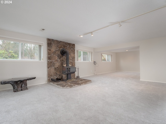 unfurnished living room featuring rail lighting, carpet floors, and a wood stove