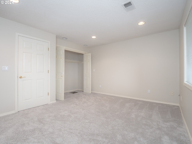 unfurnished bedroom with a textured ceiling, light carpet, and a closet