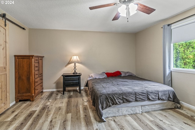 bedroom featuring a textured ceiling, light hardwood / wood-style floors, ceiling fan, and a barn door