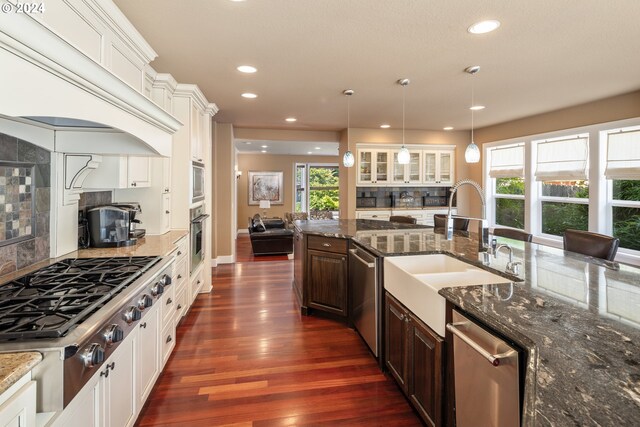 kitchen featuring hanging light fixtures, stainless steel appliances, dark brown cabinetry, sink, and backsplash