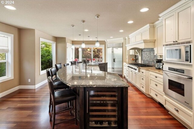 kitchen featuring built in appliances, hanging light fixtures, wine cooler, backsplash, and a large island with sink