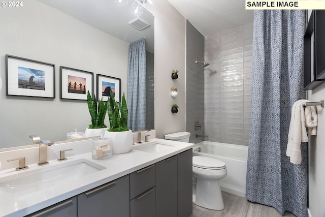 full bathroom featuring hardwood / wood-style floors, dual vanity, shower / bath combo with shower curtain, a textured ceiling, and toilet