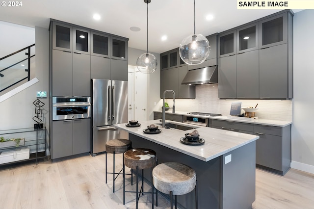 kitchen featuring light hardwood / wood-style floors, decorative backsplash, a center island with sink, and stainless steel appliances