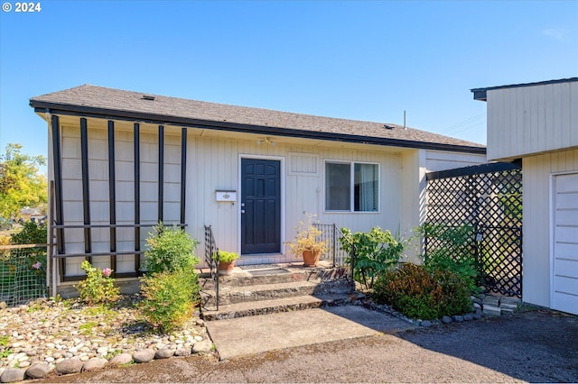 doorway to property featuring roof with shingles and fence