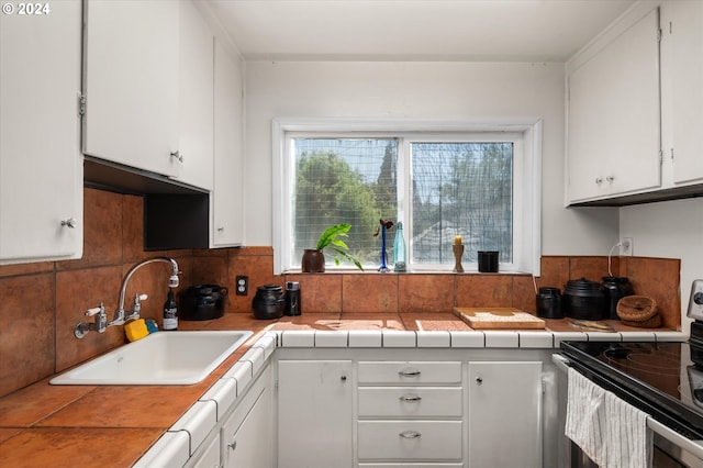 kitchen with tasteful backsplash, electric stove, tile countertops, white cabinetry, and a sink