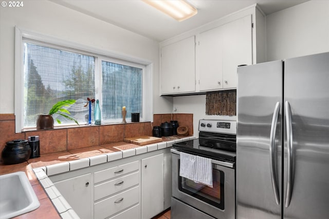 kitchen featuring white cabinets, tile countertops, stainless steel appliances, and a sink