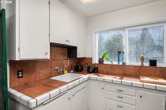 kitchen featuring backsplash, tile counters, white cabinets, and a sink