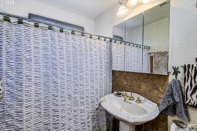 bathroom featuring curtained shower, visible vents, a sink, and tile walls