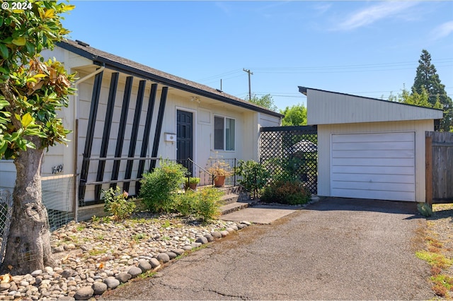 view of front of house with driveway, an outdoor structure, fence, and a detached garage