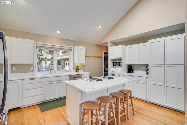 kitchen featuring lofted ceiling, stainless steel appliances, white cabinetry, a center island, and a kitchen bar