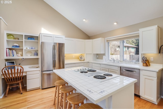 kitchen with lofted ceiling, stainless steel appliances, a sink, white cabinets, and built in desk