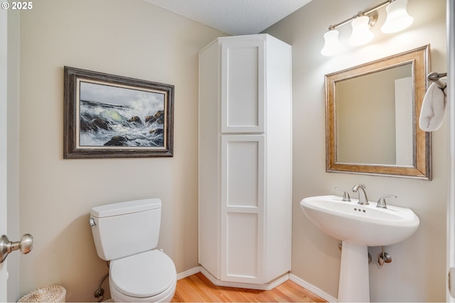 half bathroom featuring toilet, baseboards, and wood finished floors