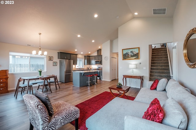 living room with an inviting chandelier, sink, high vaulted ceiling, and light hardwood / wood-style floors