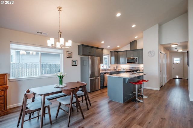 kitchen with light stone countertops, a center island, stainless steel appliances, decorative light fixtures, and hardwood / wood-style flooring