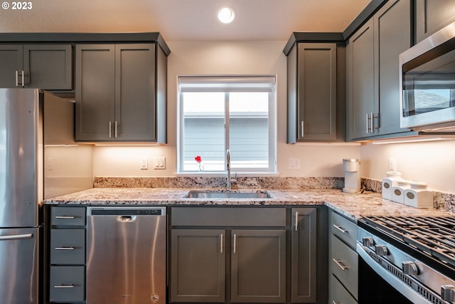 kitchen featuring gray cabinetry, light stone counters, stainless steel appliances, and sink