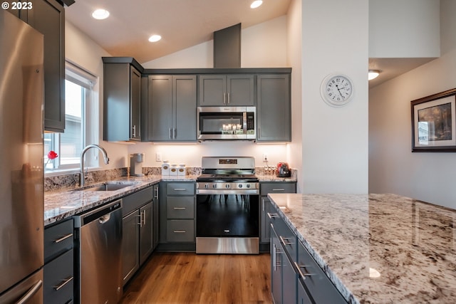 kitchen with light stone counters, lofted ceiling, appliances with stainless steel finishes, and sink