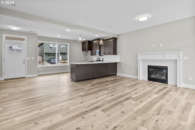 kitchen featuring dark brown cabinets, kitchen peninsula, a brick fireplace, hanging light fixtures, and light wood-type flooring