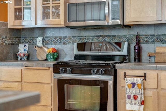 kitchen with light brown cabinetry, stainless steel appliances, and tasteful backsplash