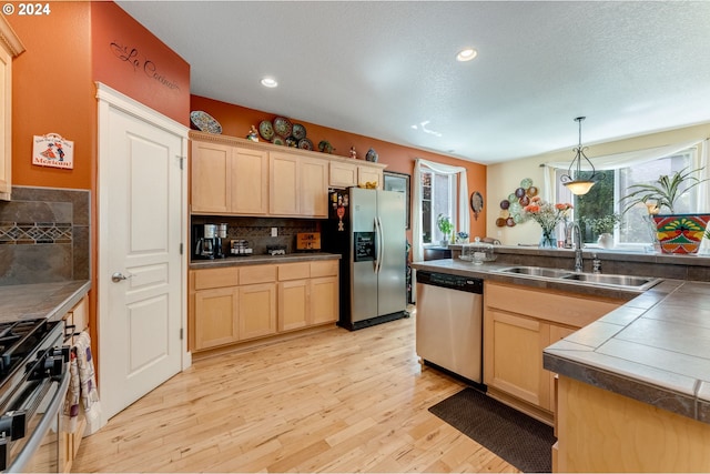 kitchen featuring tile counters, sink, hanging light fixtures, light hardwood / wood-style flooring, and appliances with stainless steel finishes